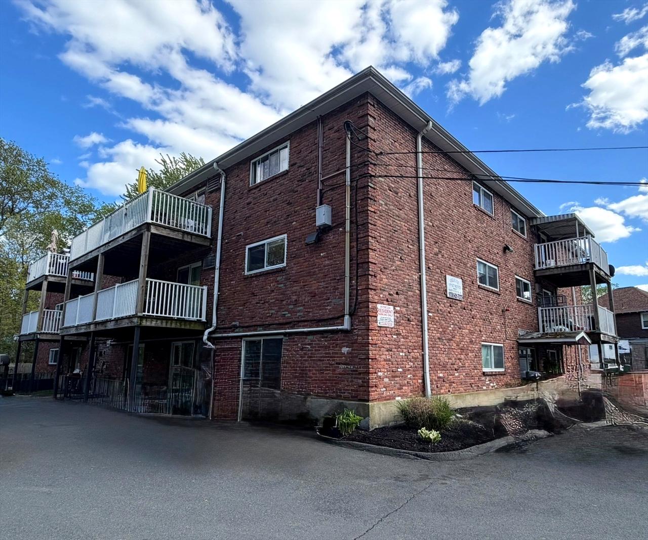 38 Clapp Street, an 18-unit brick garden-style apartment building in Malden's Linden neighborhood, shown in a three-quarter corner view with stacked wood balconies and open sky